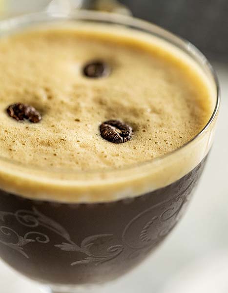 Coffee beans sitting in the foam of a cocktail