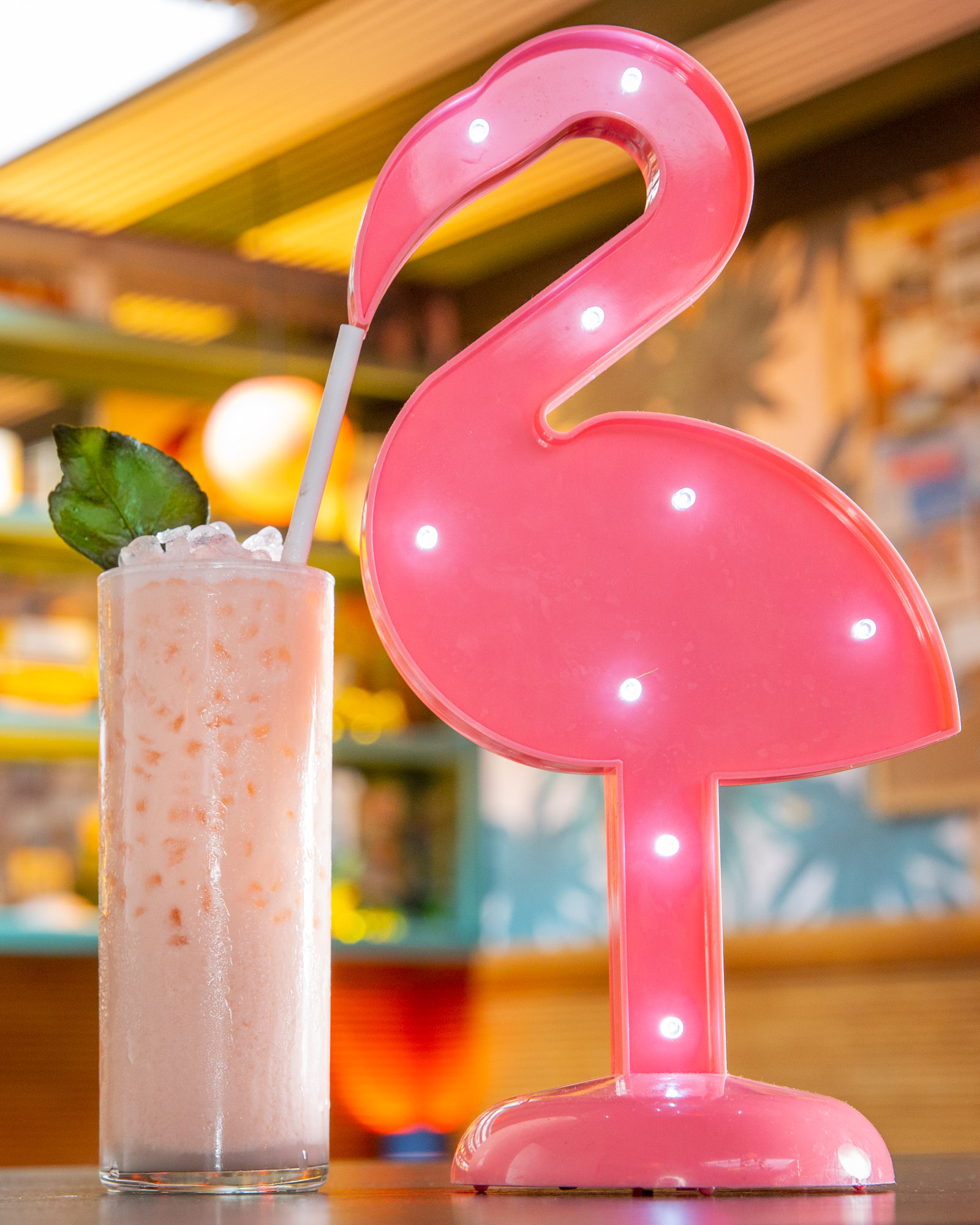 A pink plastic flamingo drinking a cocktail